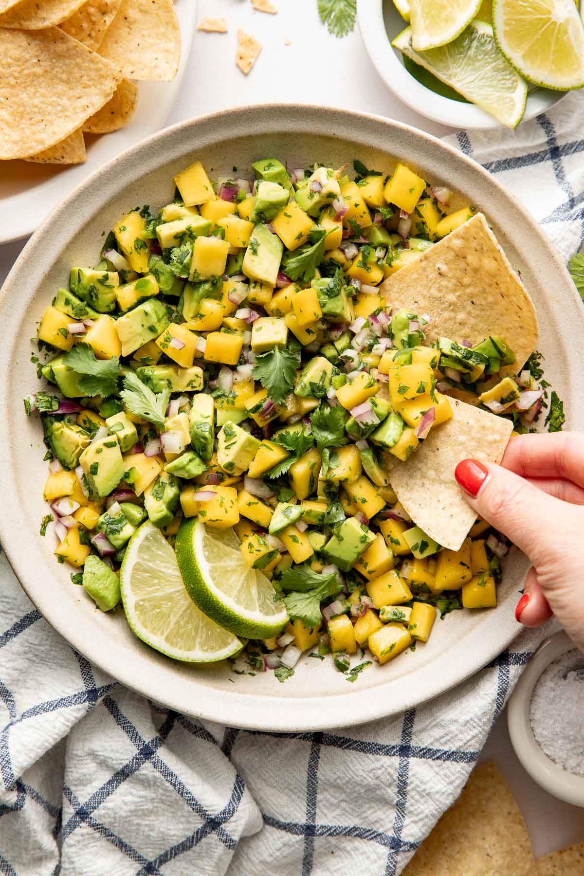 Close up view of a bowl of fresh Mango Salsa with a hand scooping a tortilla chip into the mixture.