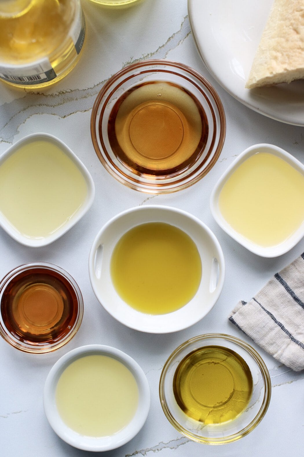 Overhead view of a variety of different cooking oils in various bowls on a white marble countertop.