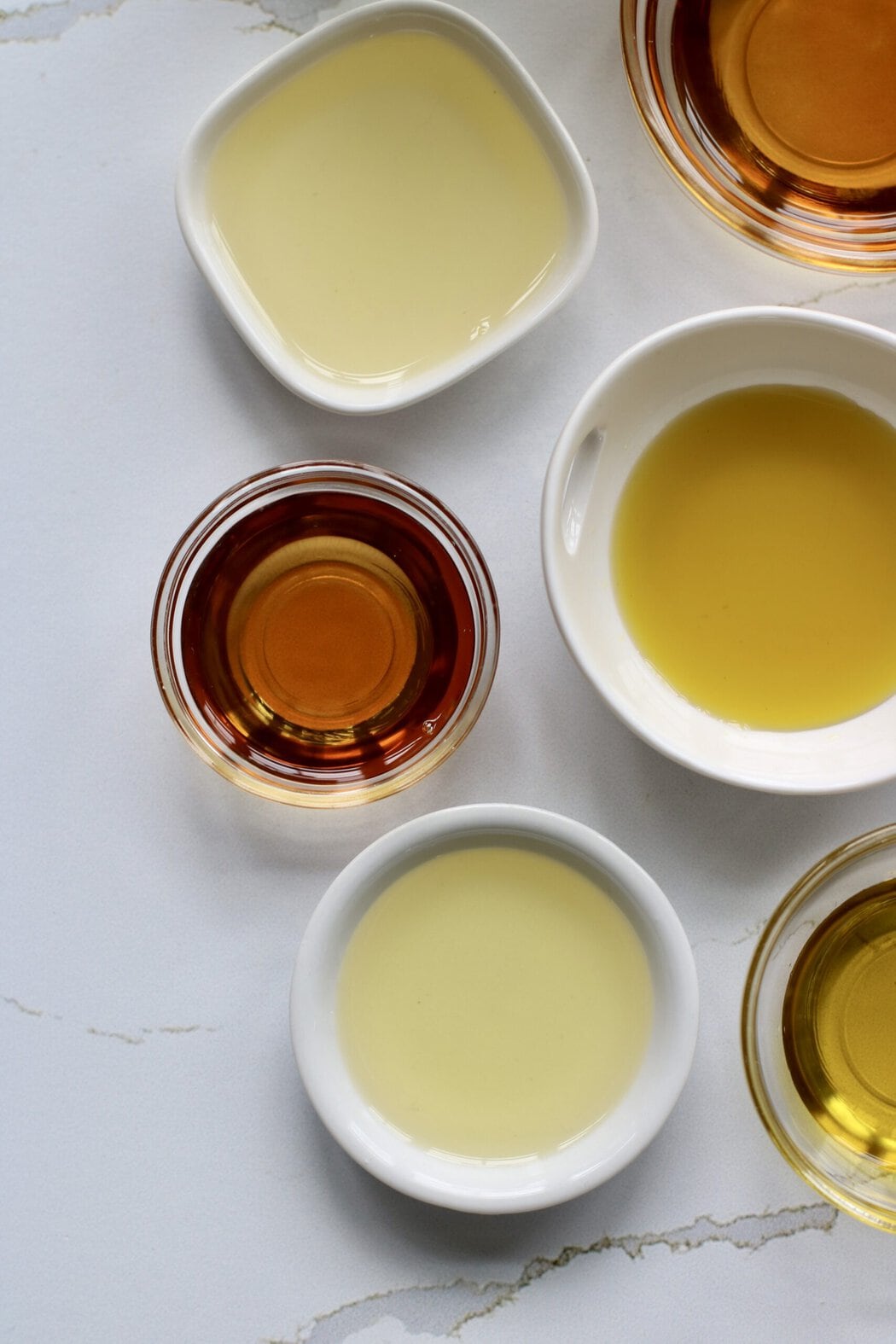 Overhead view of a variety of seed oils in different sized bowls showing different colors.