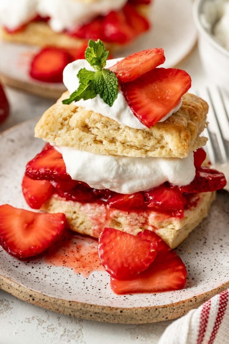Close up view of a layered Strawberry Shortcake topped with whipped cream and garnished with fresh mint leaves.