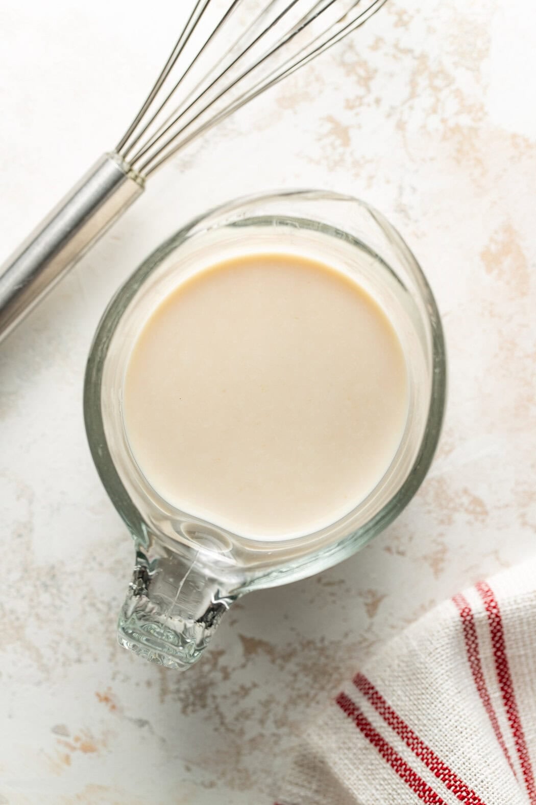 Overhead view of a measuring glass of cream on a white marble countertop.