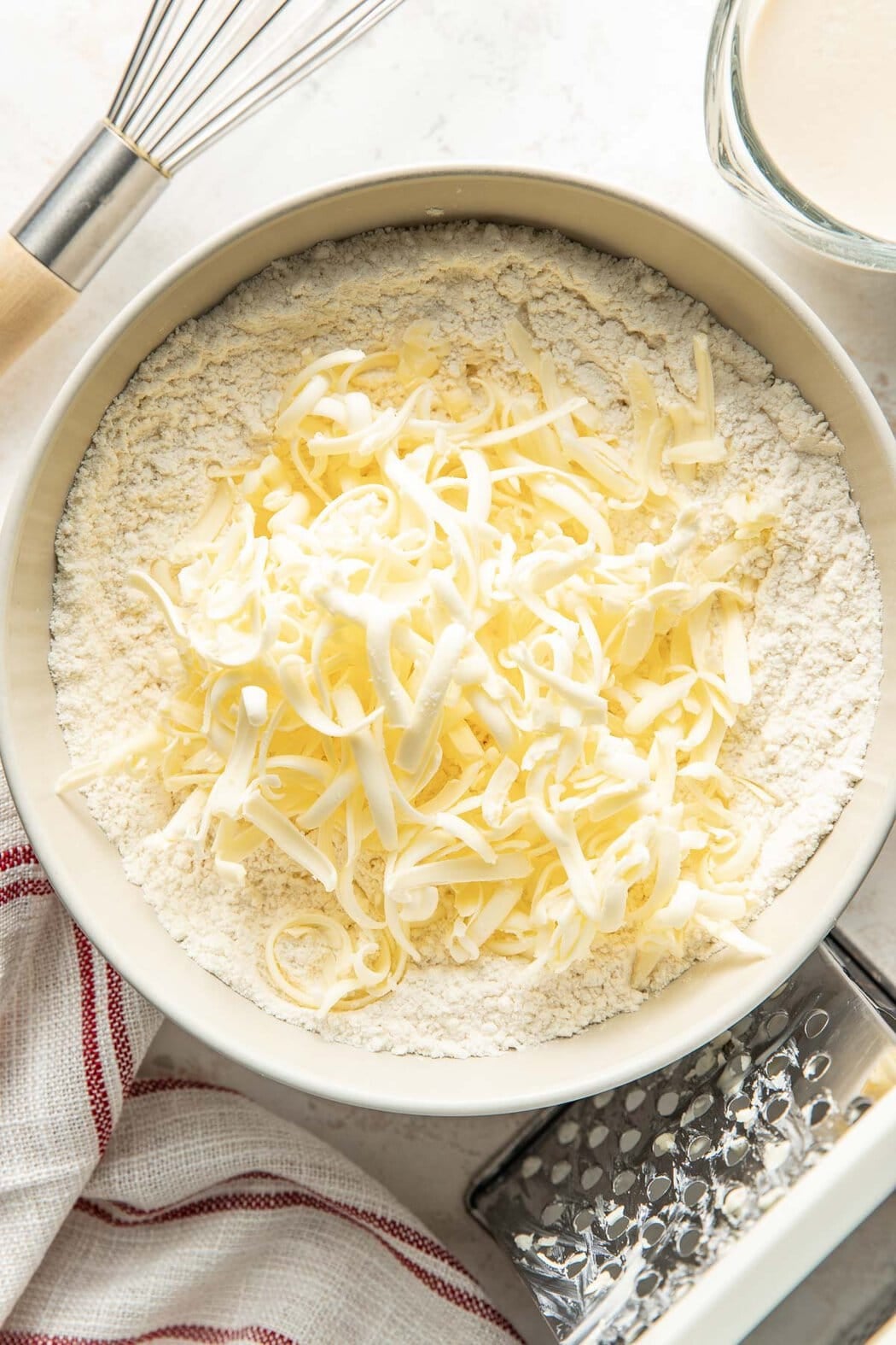 Overhead view of a bowl of flour topped with cold grated butter.