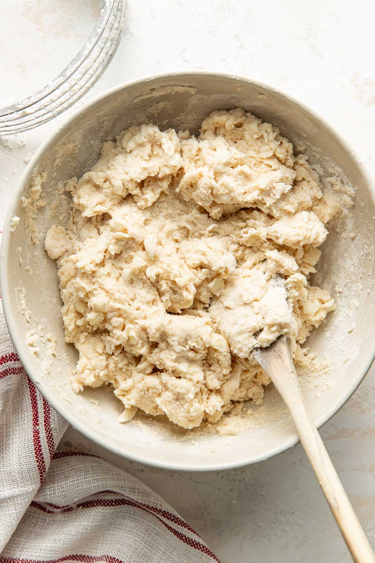 Overhead view of a bowl of sweet cream biscuit dough with a wooden spoon in the bowl.