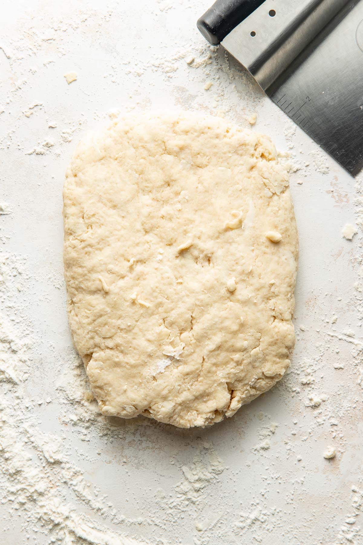 Overhead view of a piece of sweet cream biscuit dough on a floured countertop.