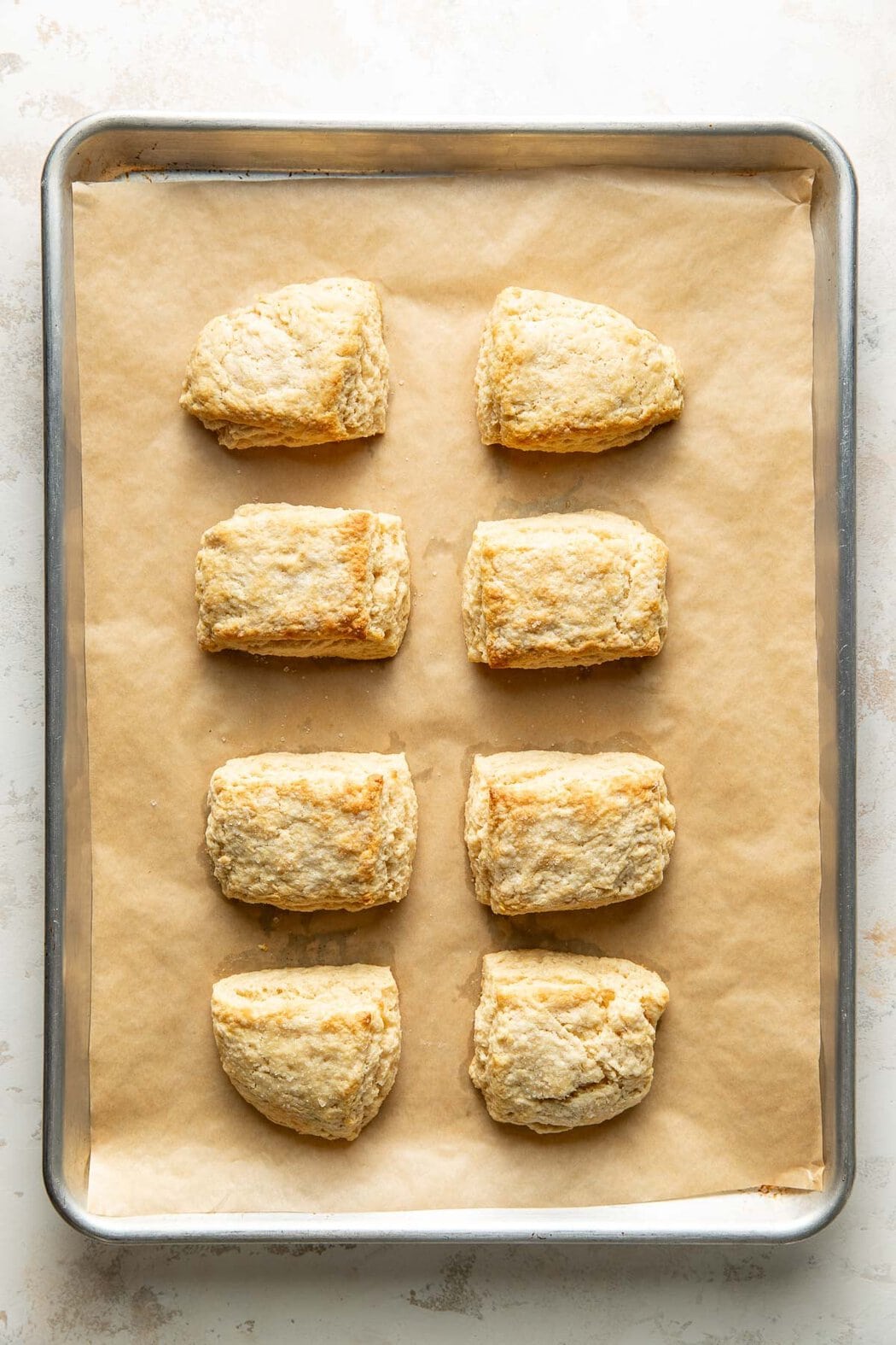 Overhead view of a parchment lined sheet pan with eight freshly baked sweet cream biscuits