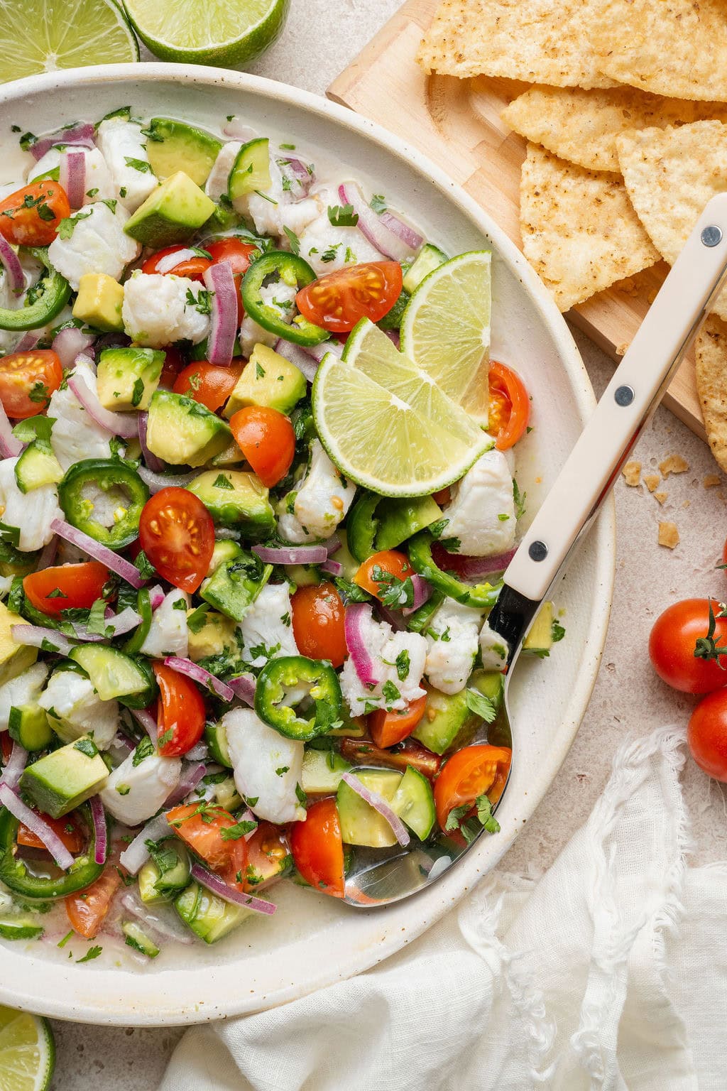 Overhead view of a bowl of fresh colorful Ceviche garnished with limes and tortilla chips surrounding the bowl. 