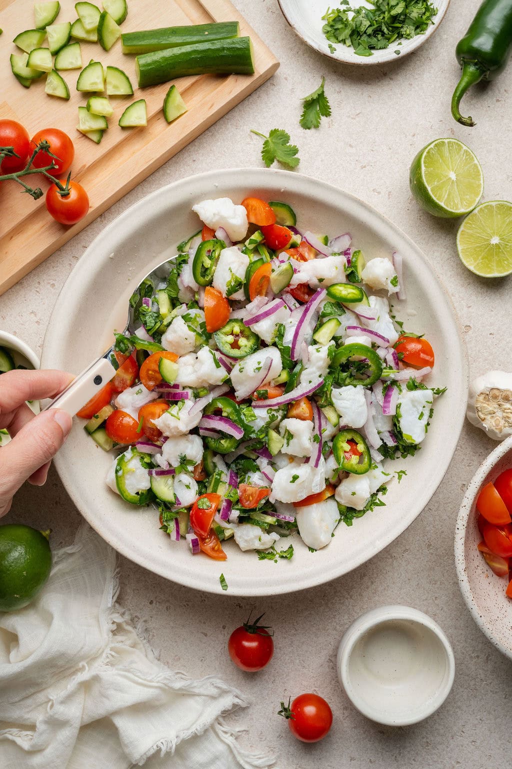 Overhead view of a fresh bowl of Ceviche being stirred with a spoon and garnished with sliced jalapeno. 