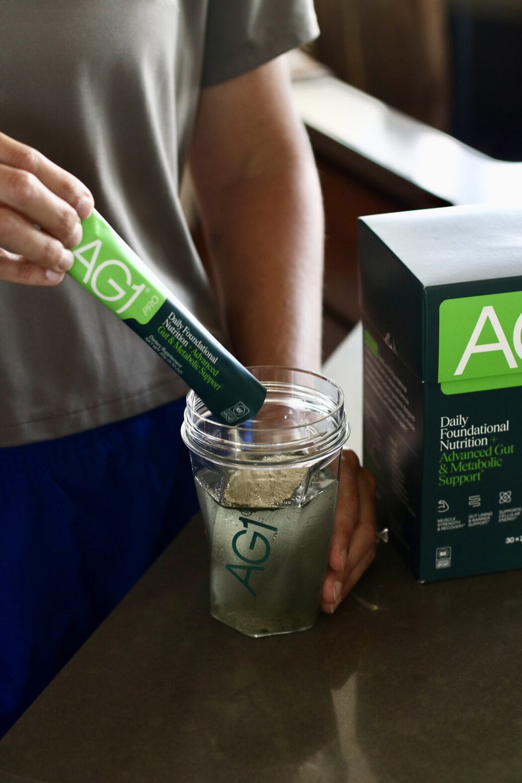 A woman pouring an AG1 Pro packet into a glass of water.