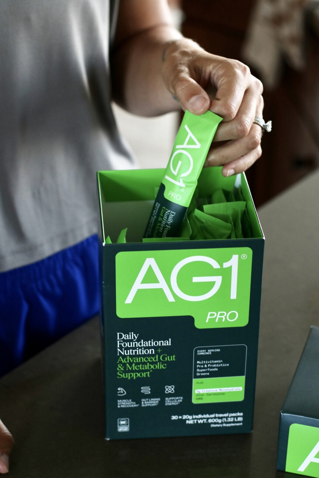 A woman's hand pulling a packet of AG1 Pro from a box.