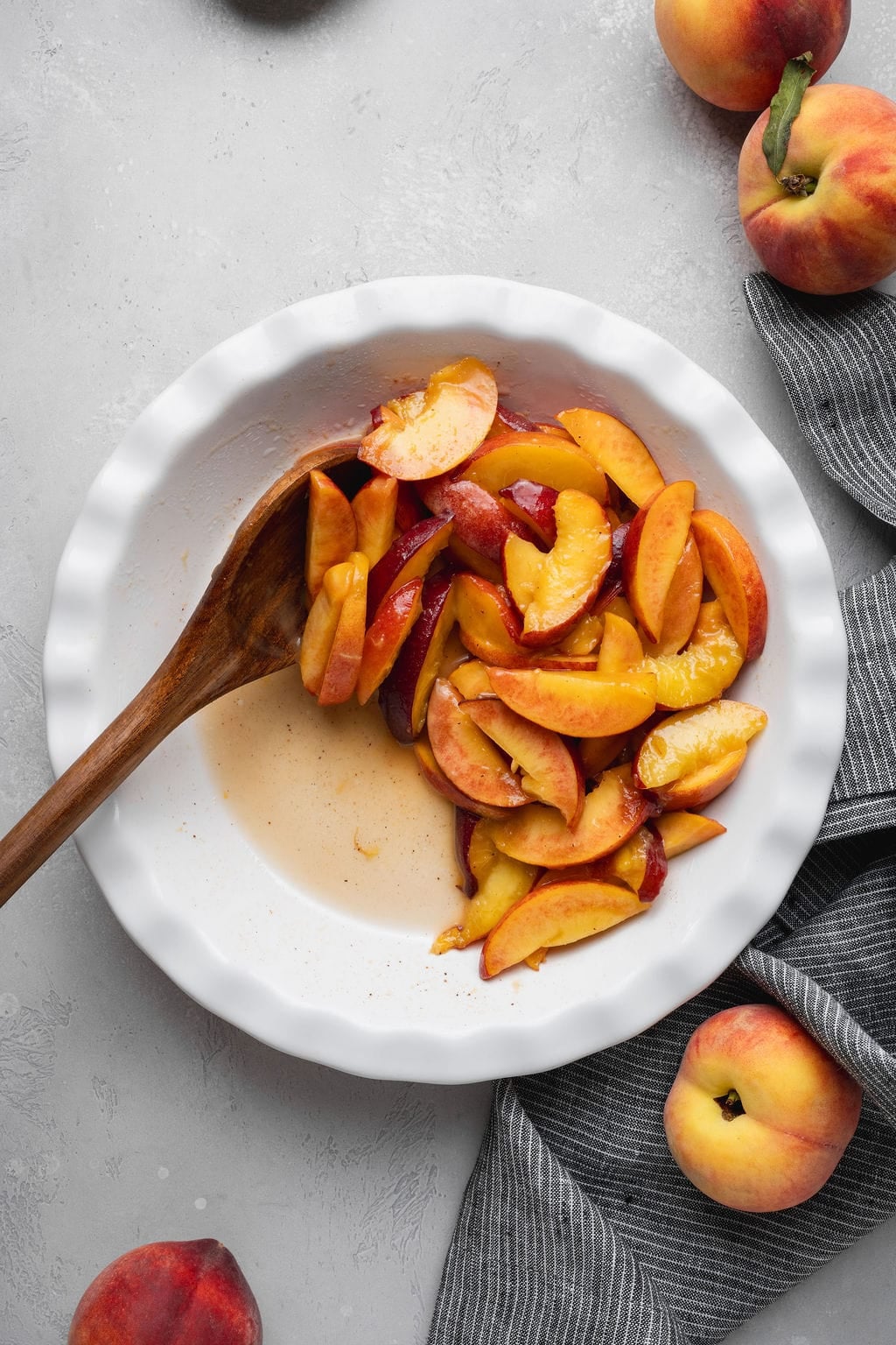 A wooden spoon stirring sliced peaches in a white bowl.