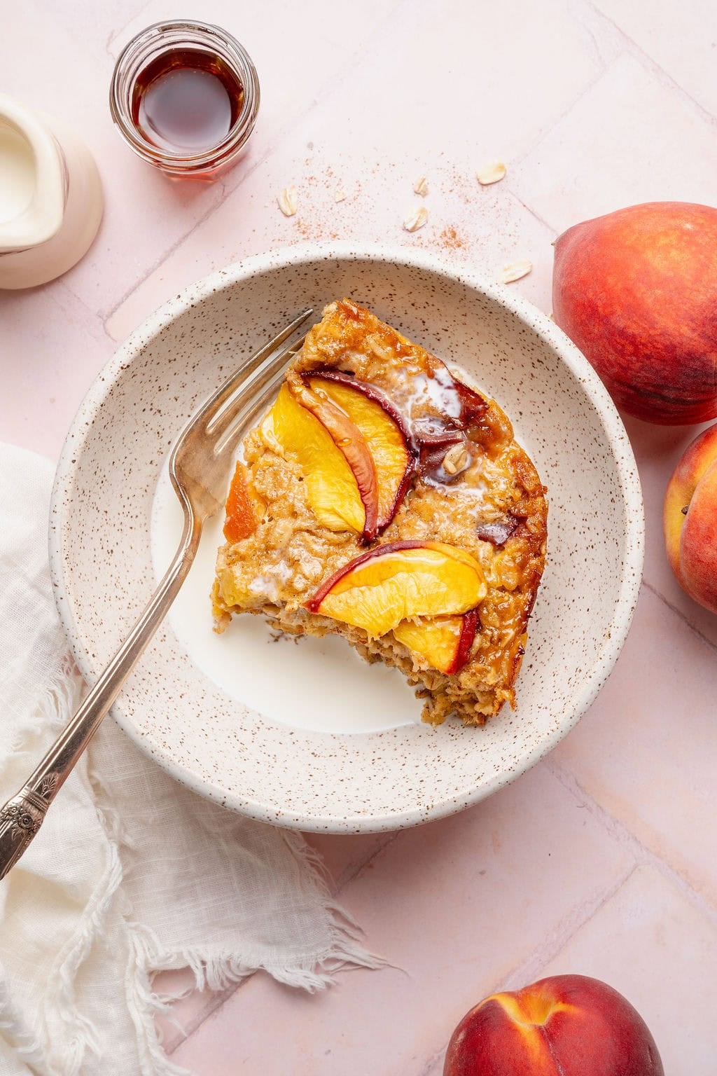 A serving of peaches and cream baked oats topped with heavy cream in a bowl, a fork on the side.
