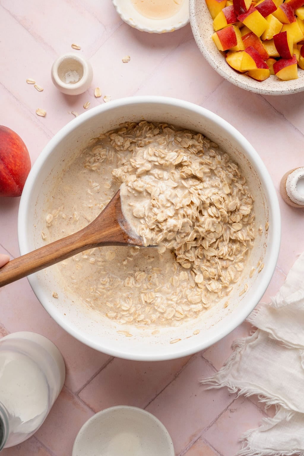 A wooden spoon stirring wet batter for peach baked oatmeal in a white bowl.
