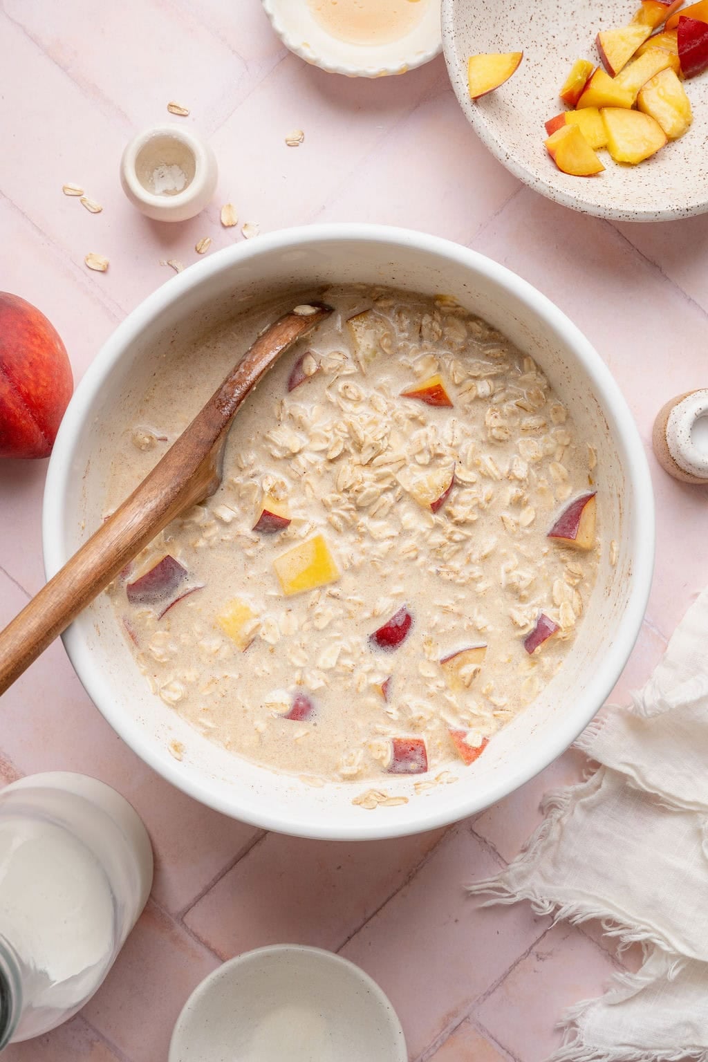 A wooden spoon stirring diced peaches into a bowl of baked oatmeal ingredients.