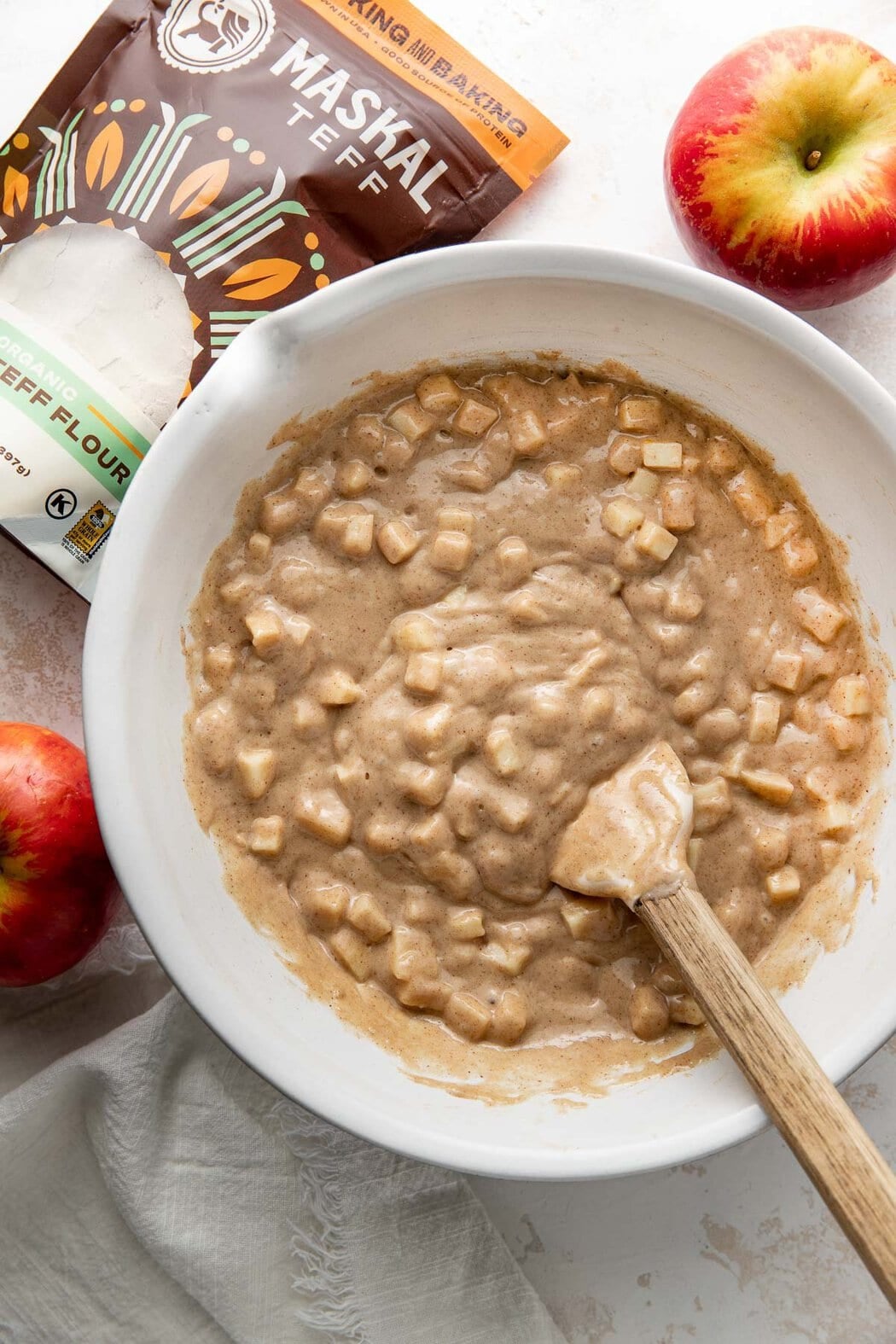Wet apple cake ingredients being mixed in a bowl, a rubber spatula sticking out.
