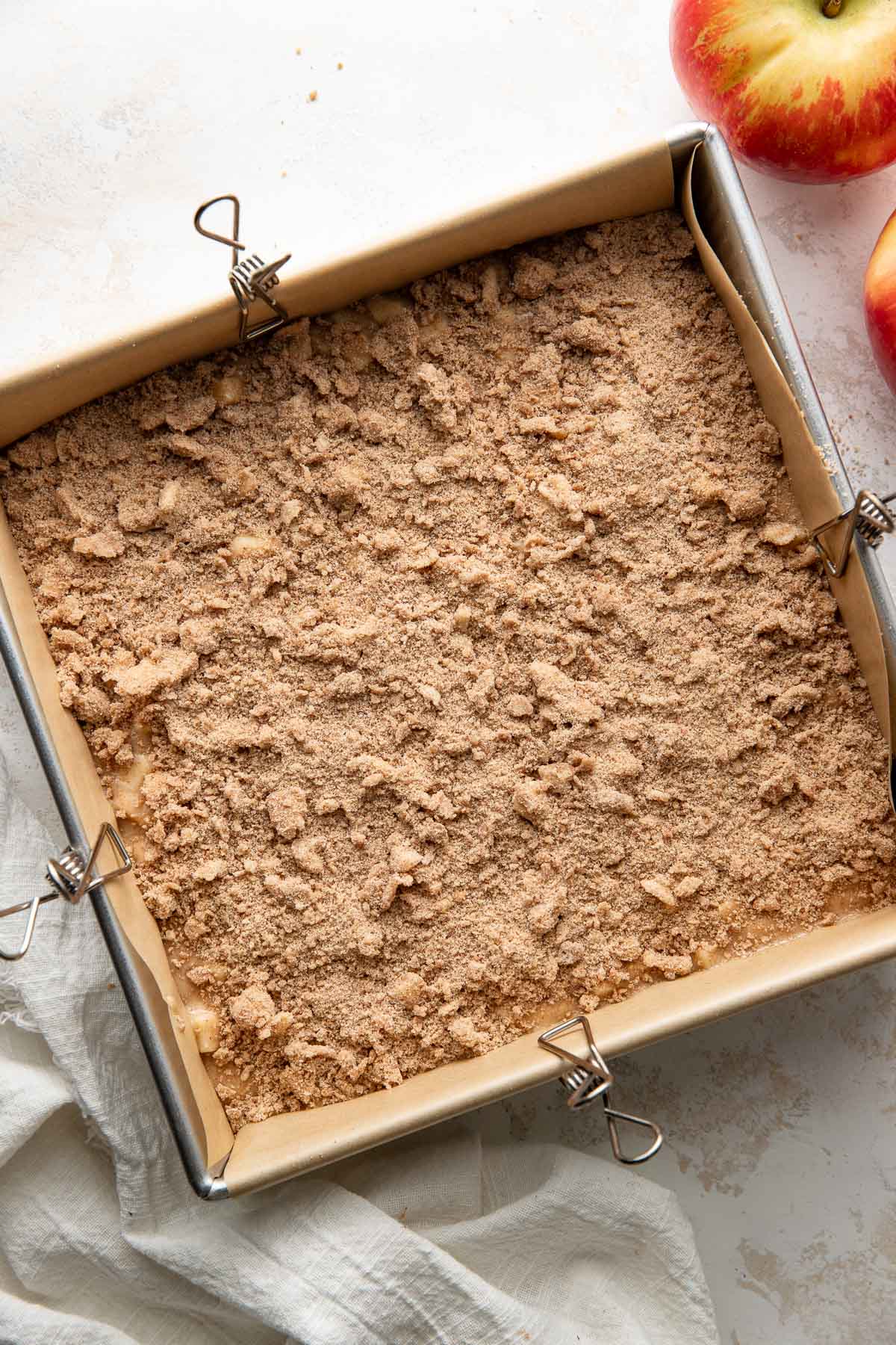An uncooked apple coffee cake in a parchment paper-lined baking dish.