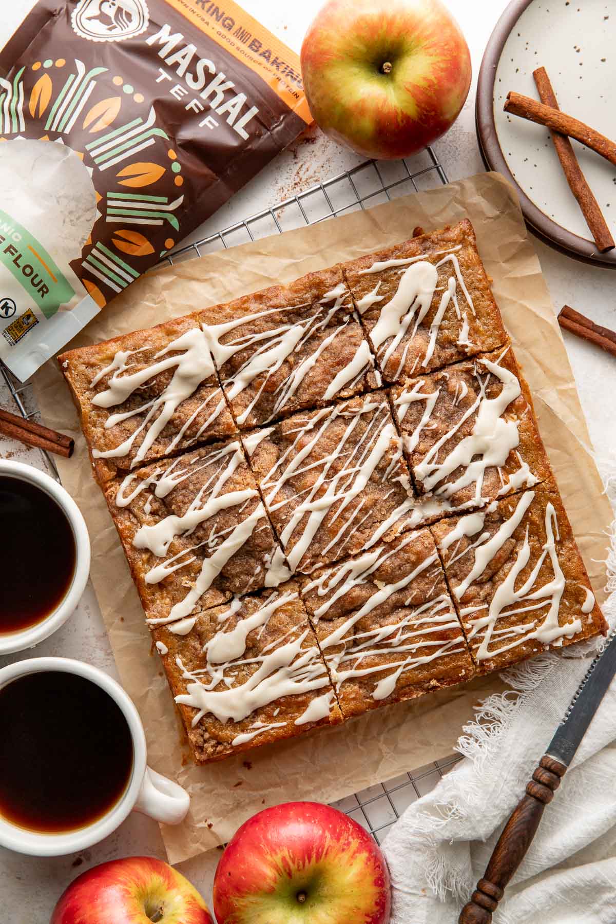 An apple coffee cake on parchment paper sliced into squares and drizzled with icing.