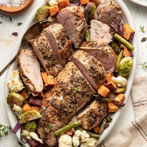 Oven roasted pork tenderloin on a platter with roasted vegetables.