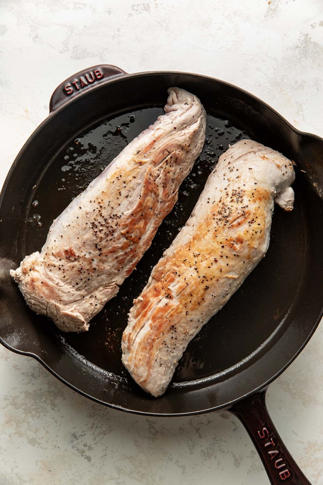 Two pork tenderloins being seared in a cast-iron skillet.
