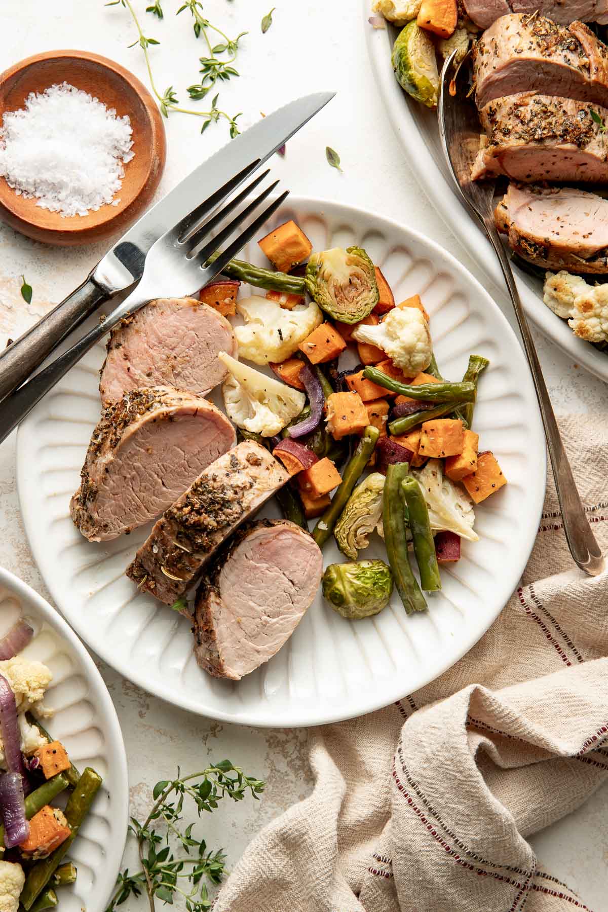 Oven roasted pork tenderloin slices and roasted vegetables on a plate, a fork and knife on the side.
