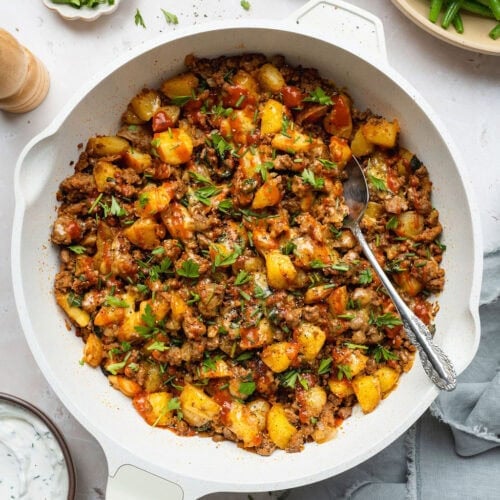 A ground beef and potatoes skillet with a spoon sticking out.