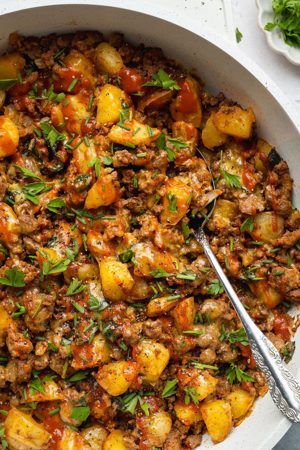 A skillet of cheesy ground beef and potatoes, a spoon digging in.