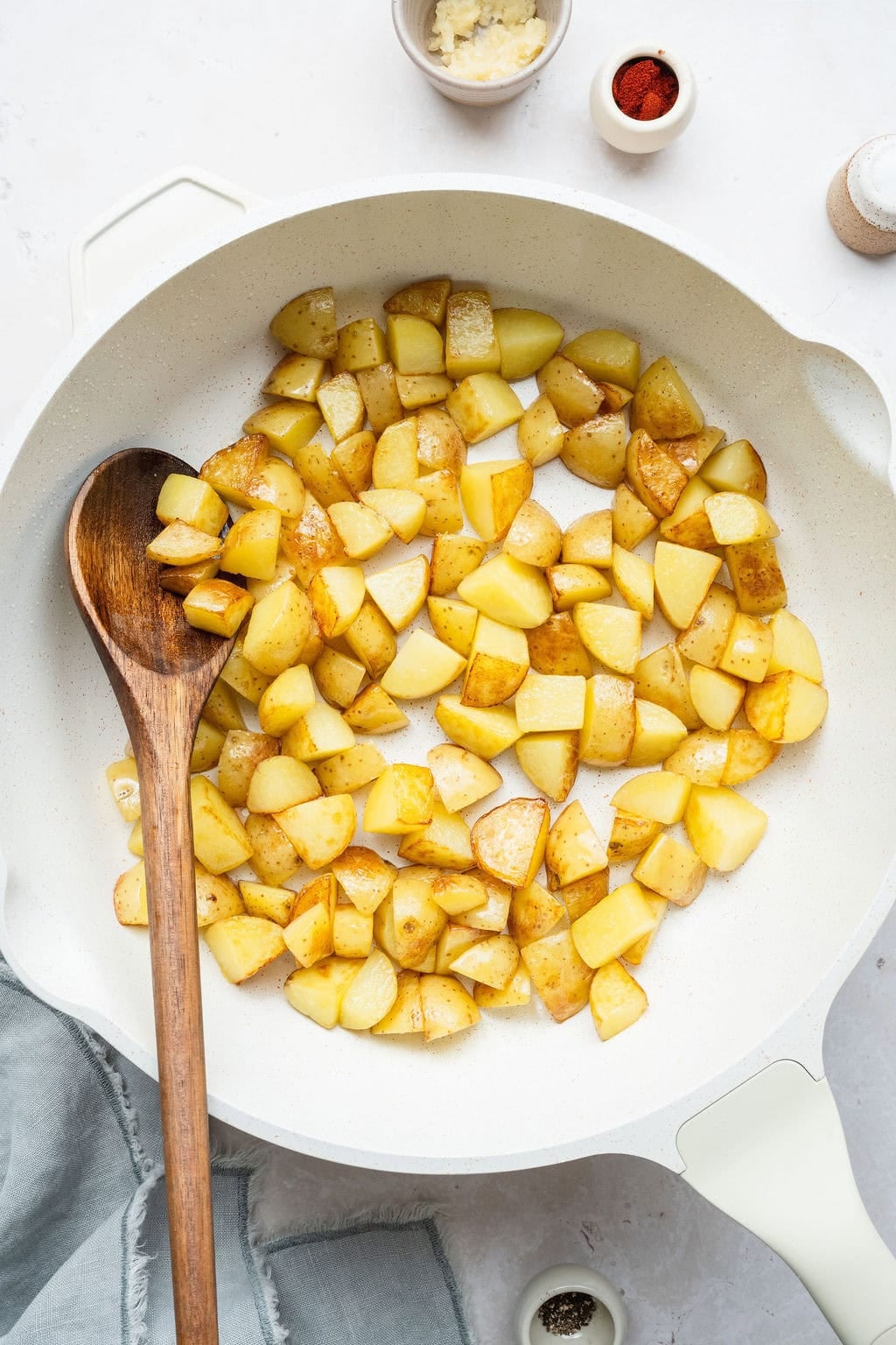 Potato pieces browning in a skillet, a wooden spoon sticking out.