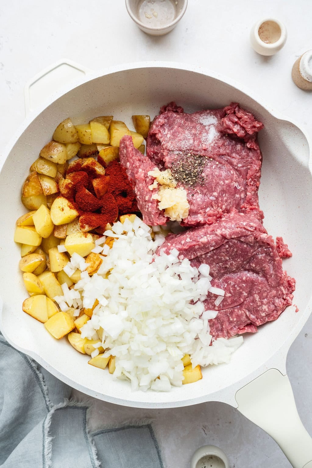 Potato pieces, raw ground beef, diced onions, and seasonings in a skillet.