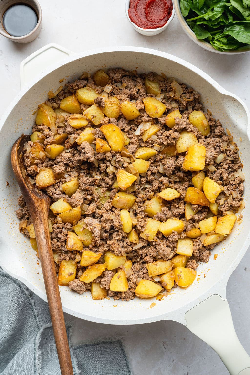 A skillet of potato pieces and browned ground beef, a wooden spoon on the side.
