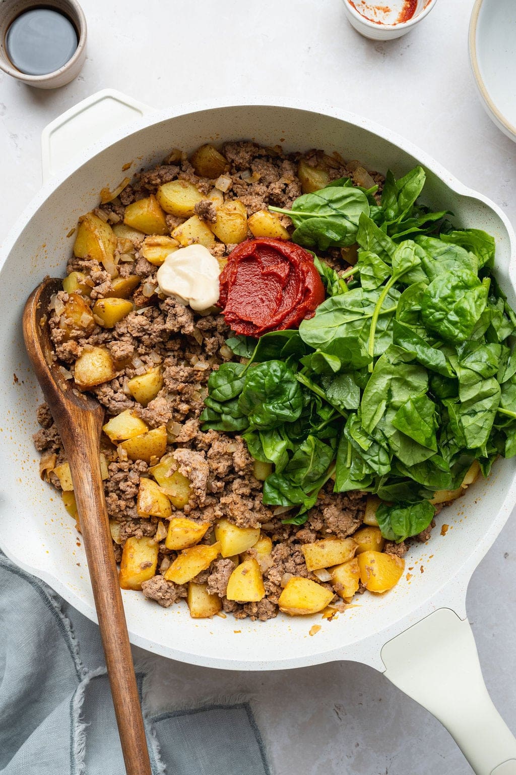 A skillet of browned ground beef, potatoes, spinach, tomato paste, and Dijon.