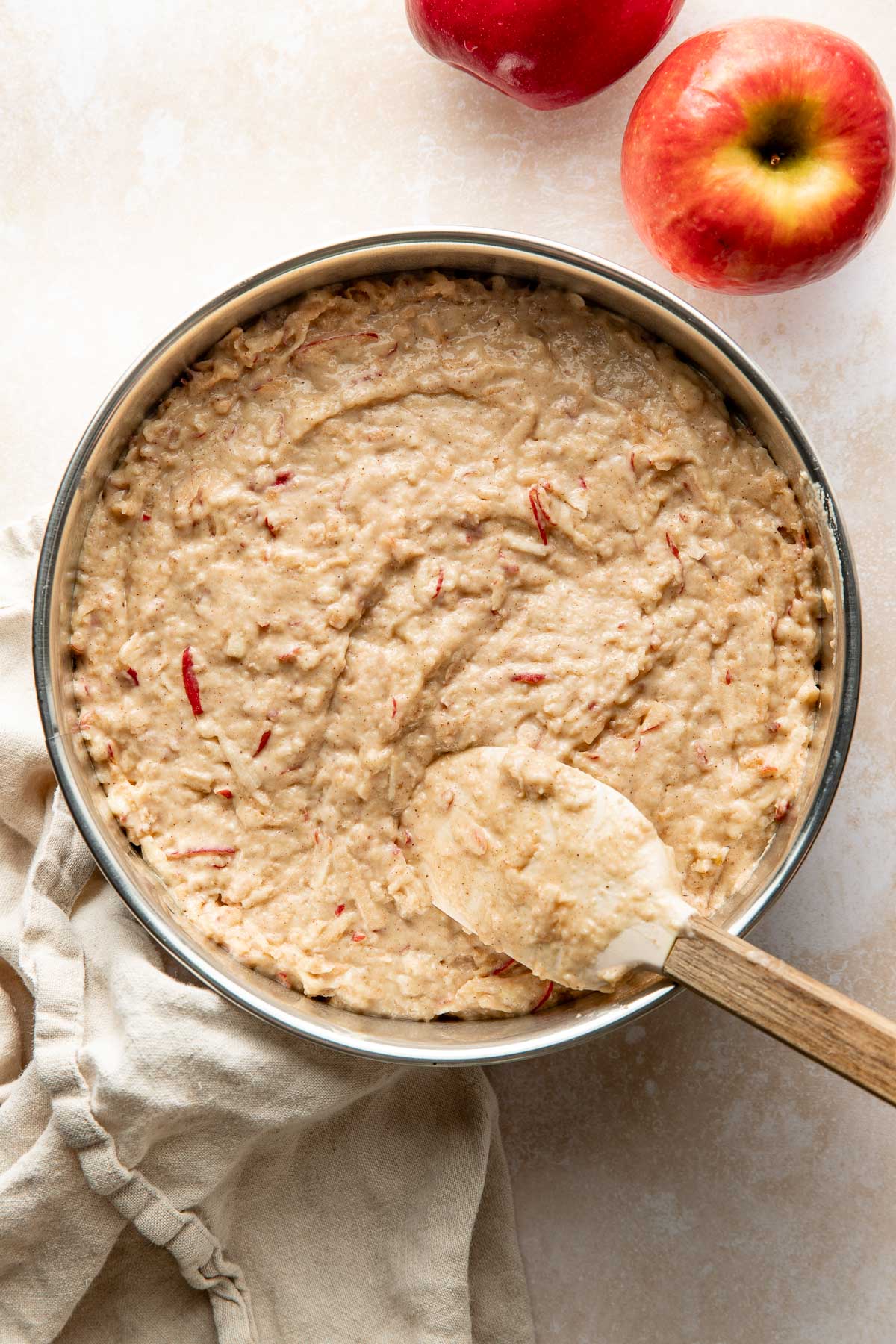 A spatula smoothing apple cake batter in a round cake pan.
