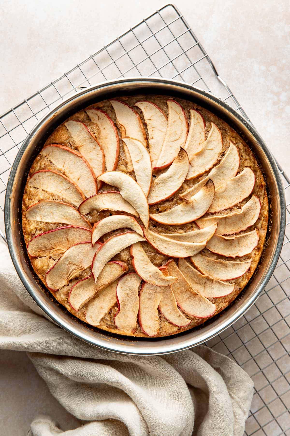 Baked apple cake topped with apple slices in a round cake pan.