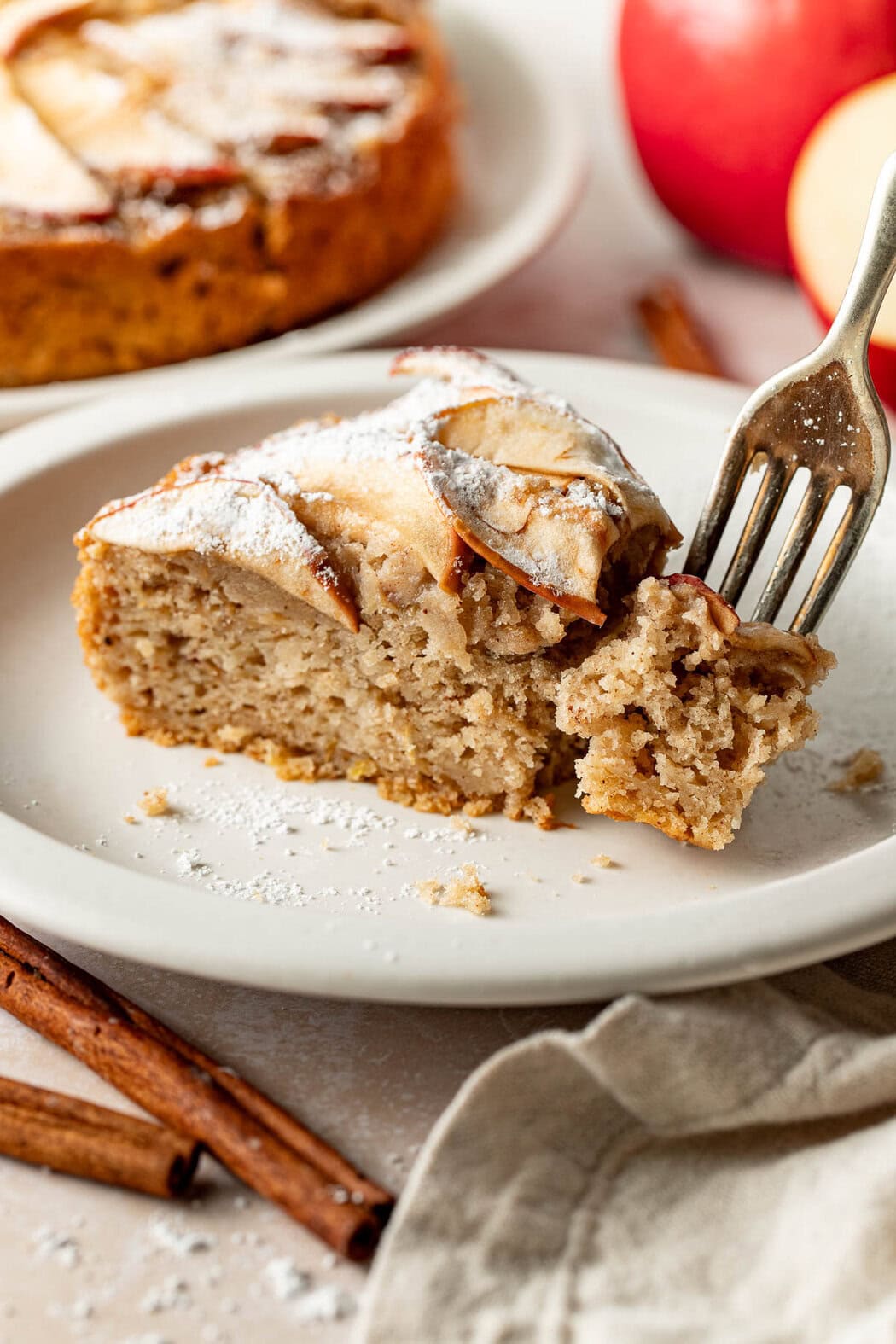 A slice of apple cake on a plate, a fork holding a bite.