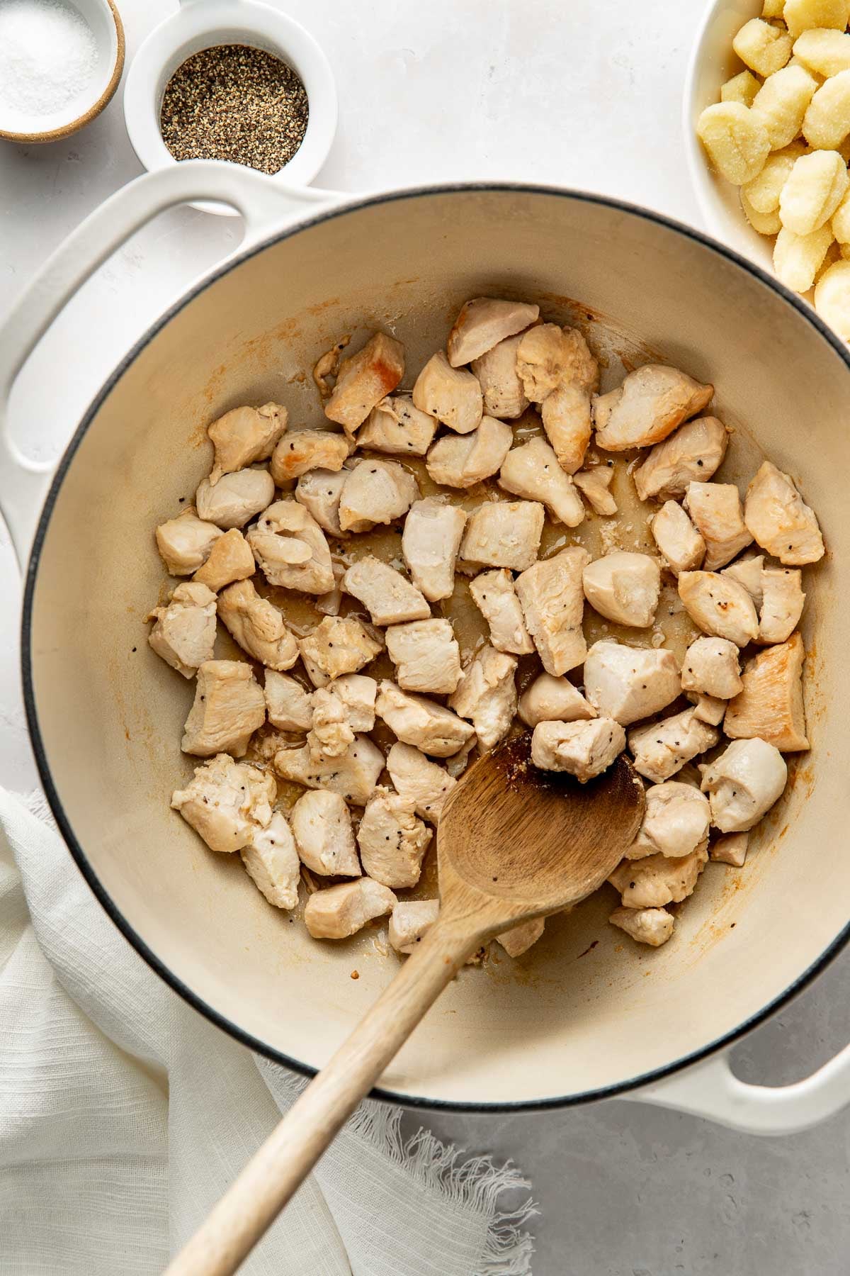 Chicken pieces cooking in a large pot, a wooden spoon sticking out.