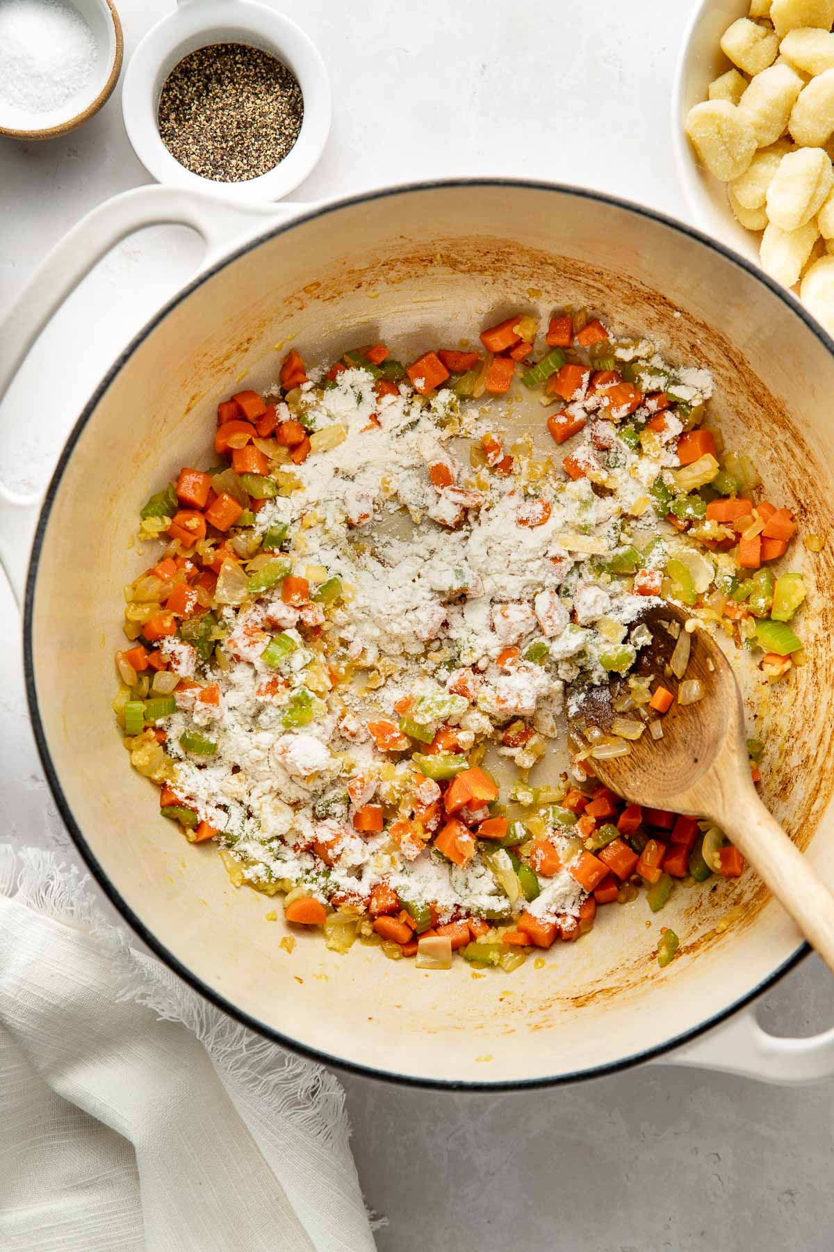 Flour being added to a sautéed mirepoix mix in a pot.