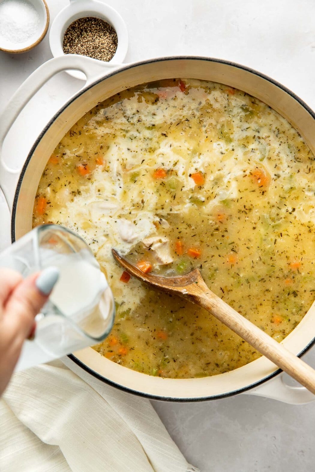 Milk being added to a pot of chicken gnocchi soup, a wooden spoon sticking out.