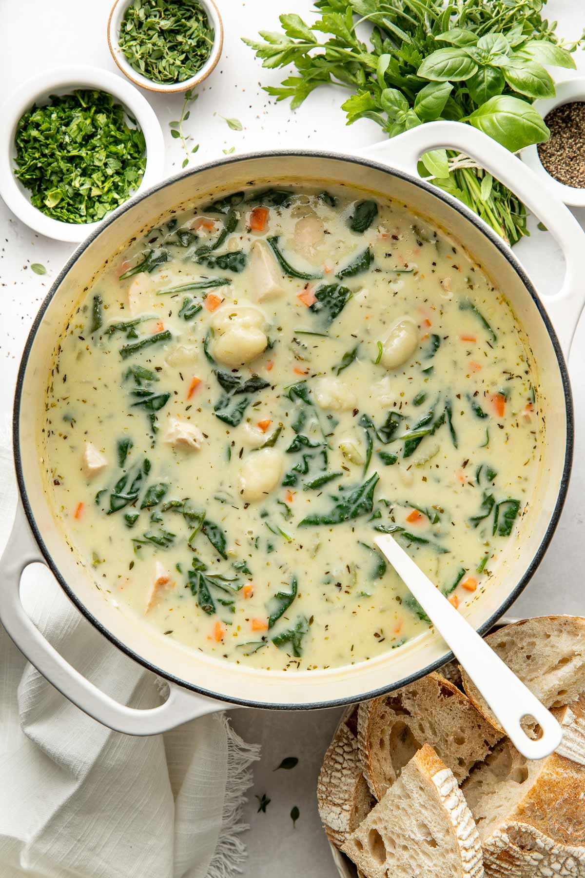 A pot of creamy chicken gnocchi soup with wilted spinach, a ladle sticking out.