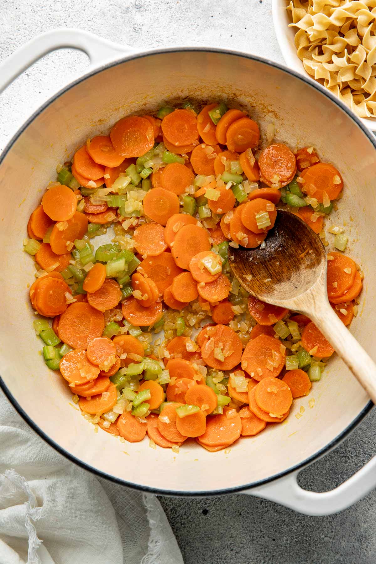 Sautéed carrots, onion, celery, and garlic in a soup pot, a wooden spoon sticking out.