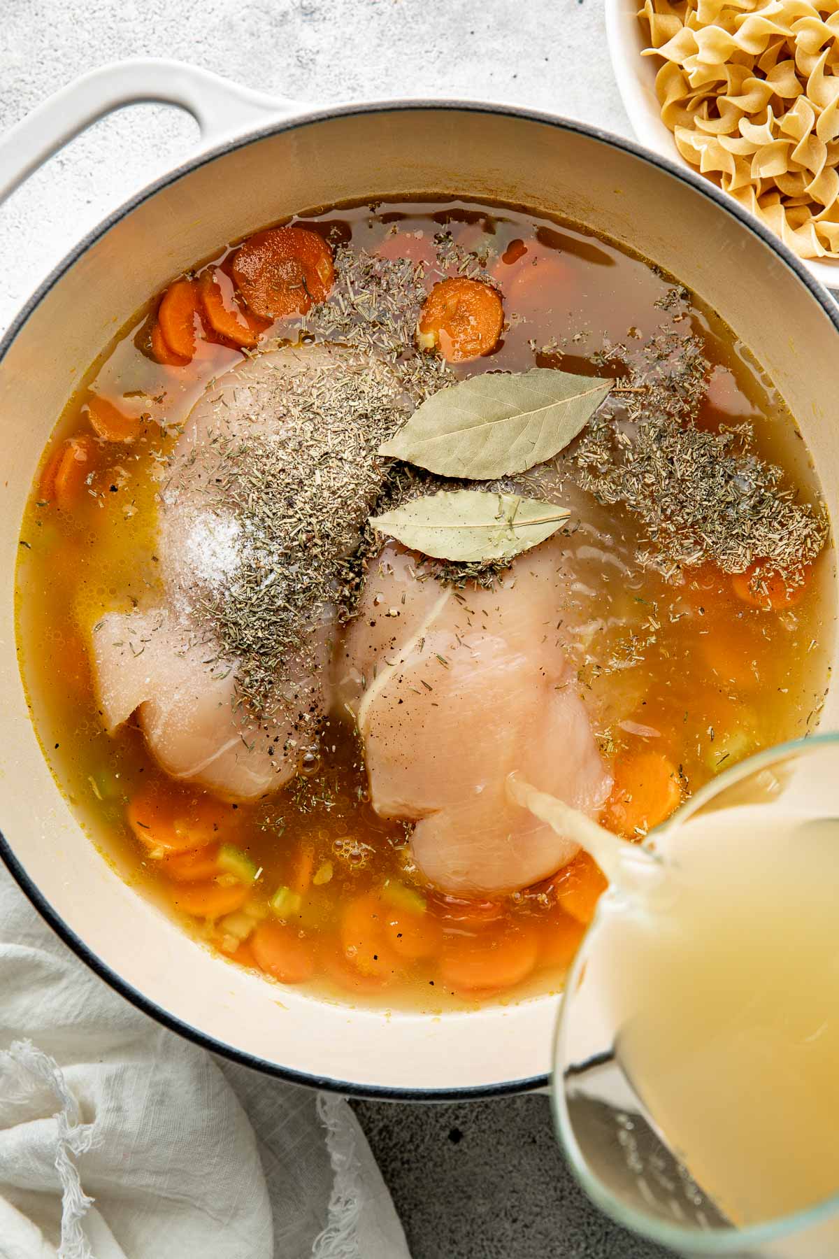 Broth being poured into a pot of ingredients to make chicken noodle soup.