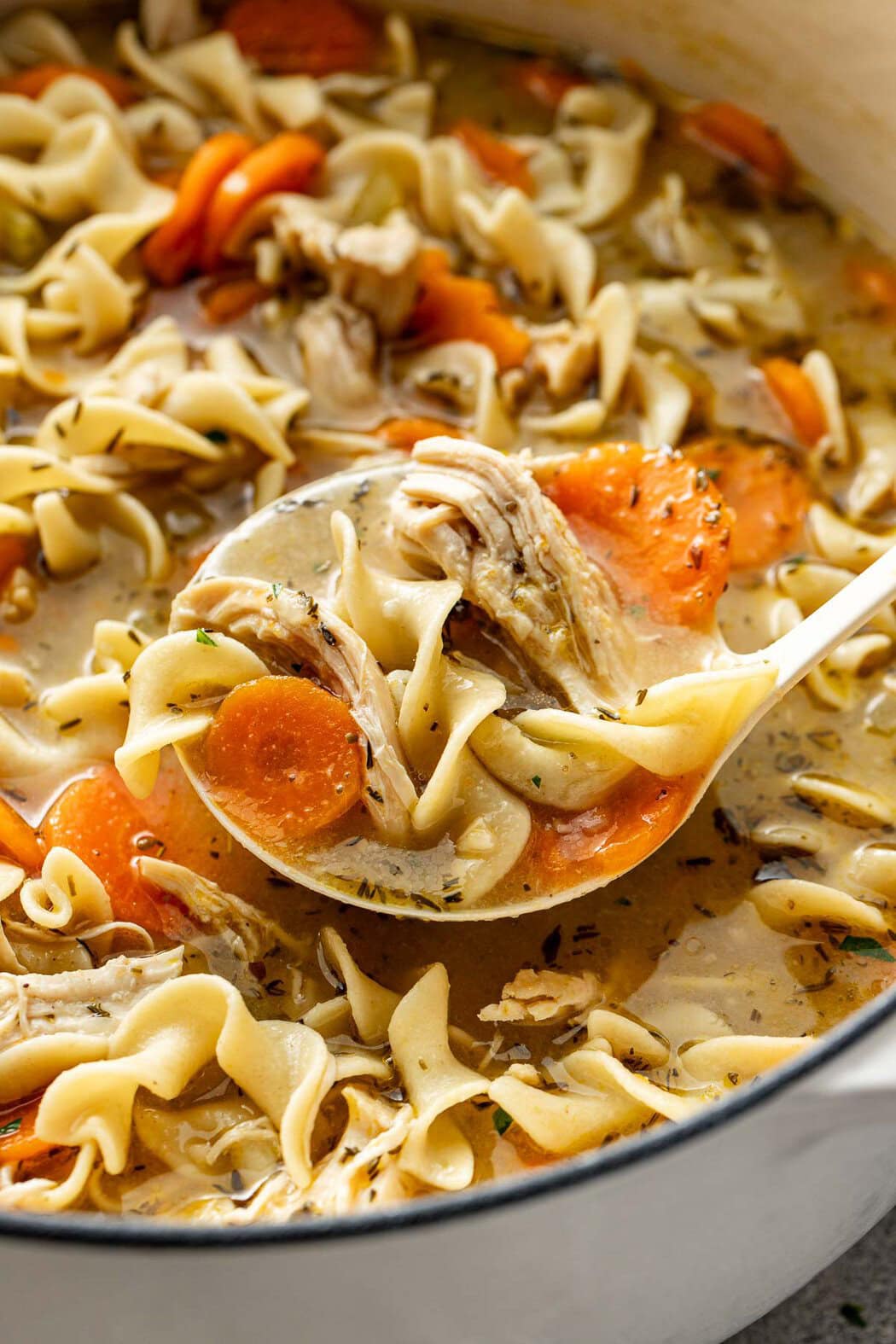 A ladle lifting a scoop of homemade chicken noodle soup from a bowl.