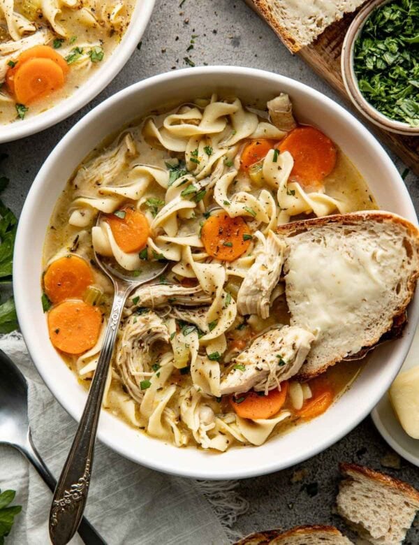 A bowl of chicken noodle soup with a piece of butter bread on the side