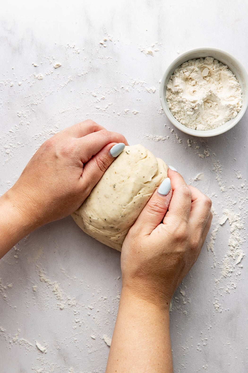 A woman's hands kneading homemade pizza dough on a white marble work surface.