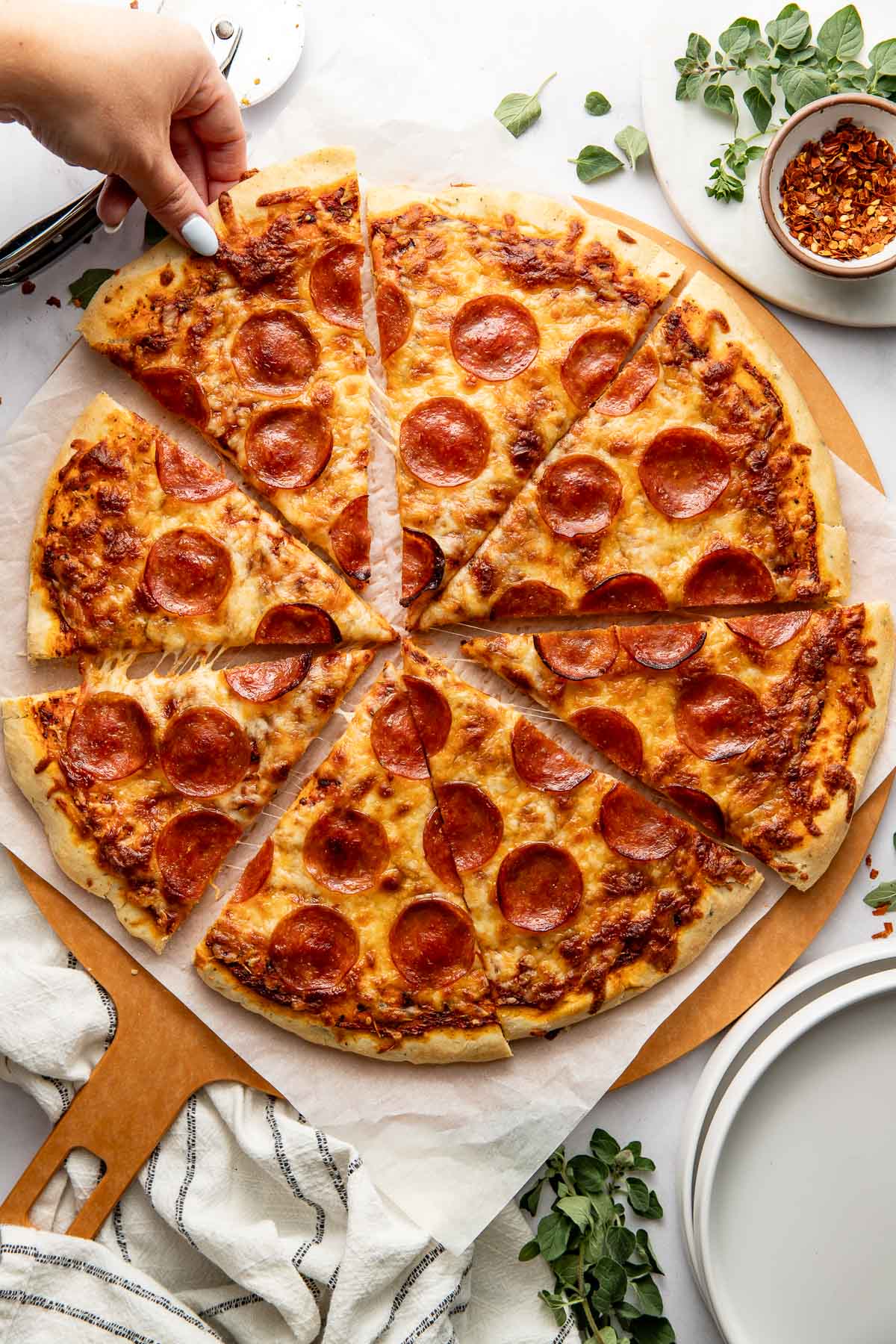 A hand grabbing a slice of pepperoni pizza from a full pizza cut into eight pieces.