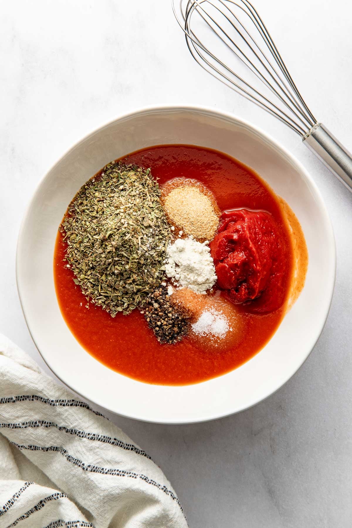 Pizza sauce ingredients in a bowl, a whisk on the side.
