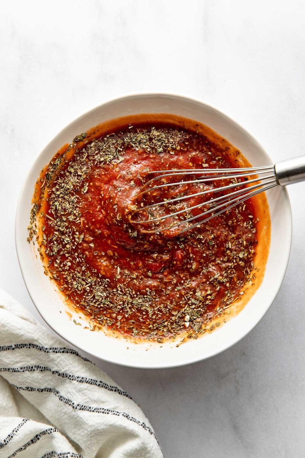 Pizza sauce ingredients being whisked in a bowl.