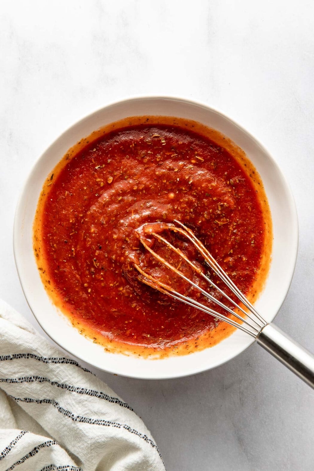 A bowl of pizza sauce, a whisk sticking out.