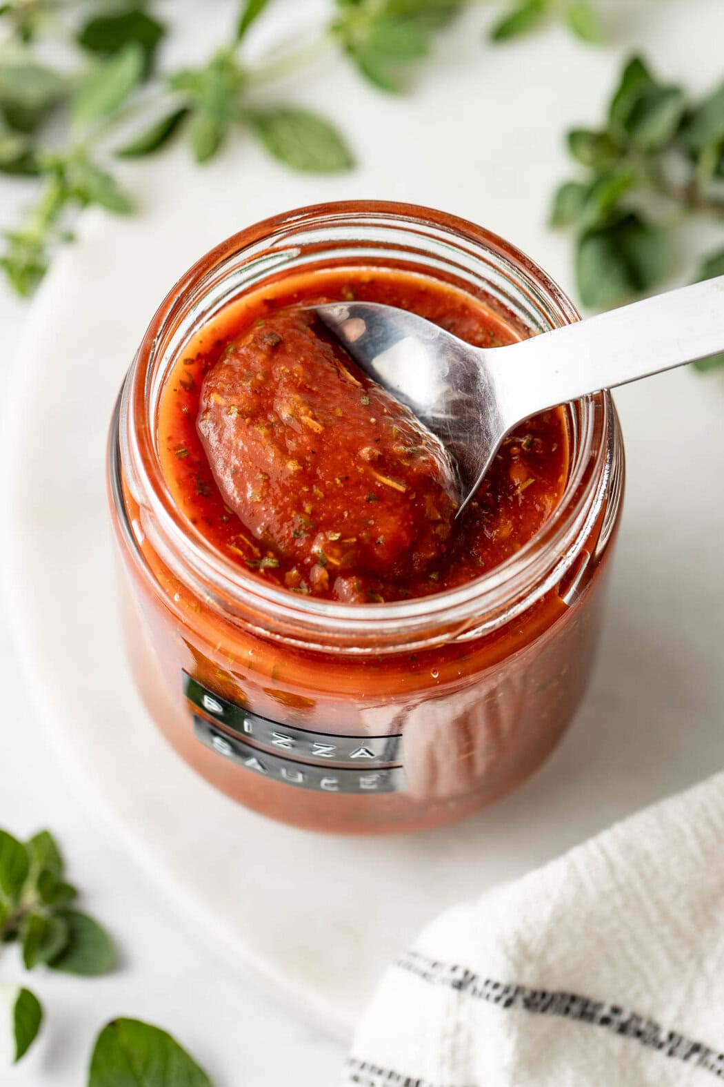 A tablespoon lifting a scoop of pizza sauce from a jar.