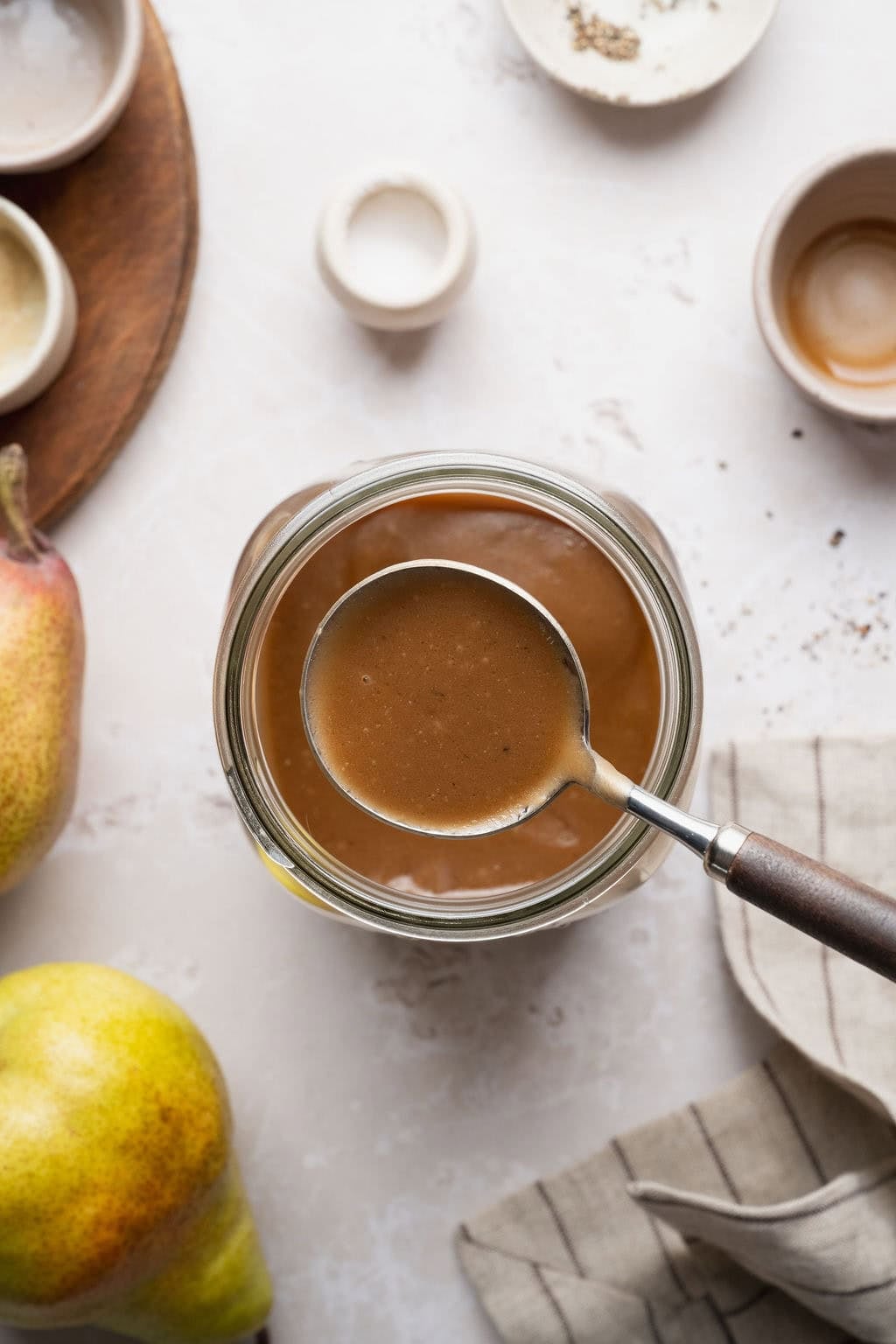 A spoon lifting a scoop of creamy balsamic vinaigrette from a large mason jar.