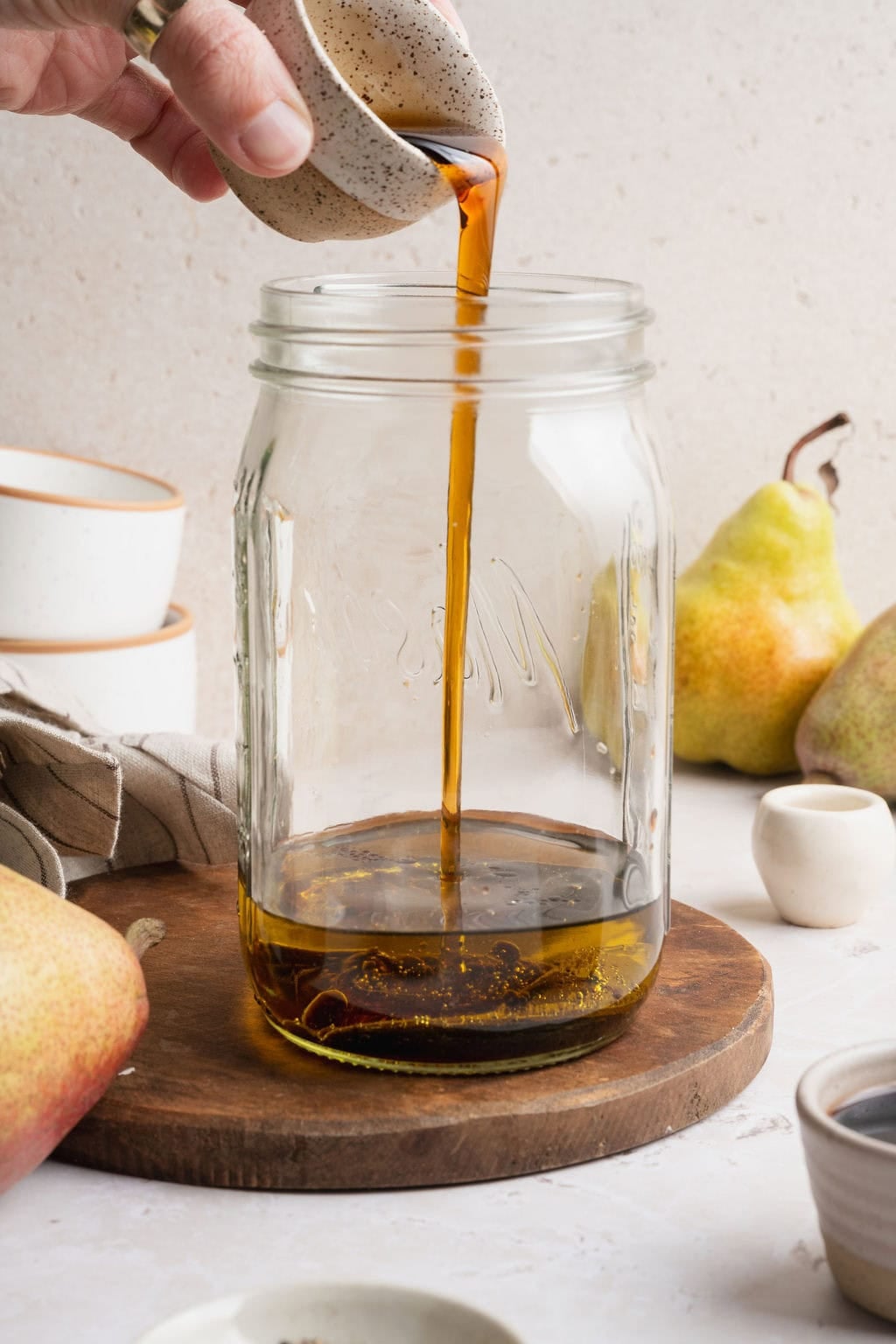Maple syrup being poured into a mason jar with olive oil and balsamic vinegar.
