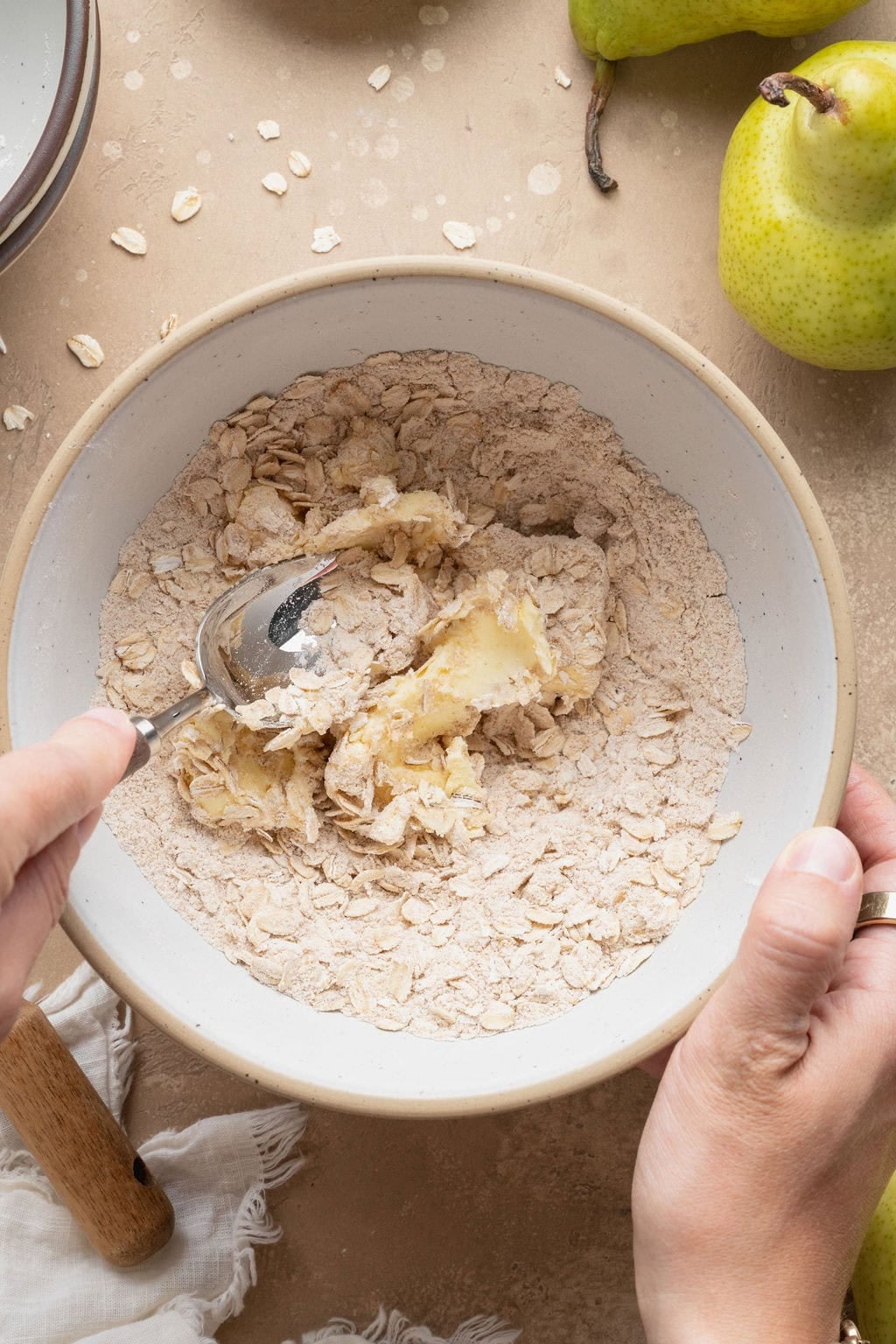 A woman stirring pear crisp topping ingredients in a bowl.
