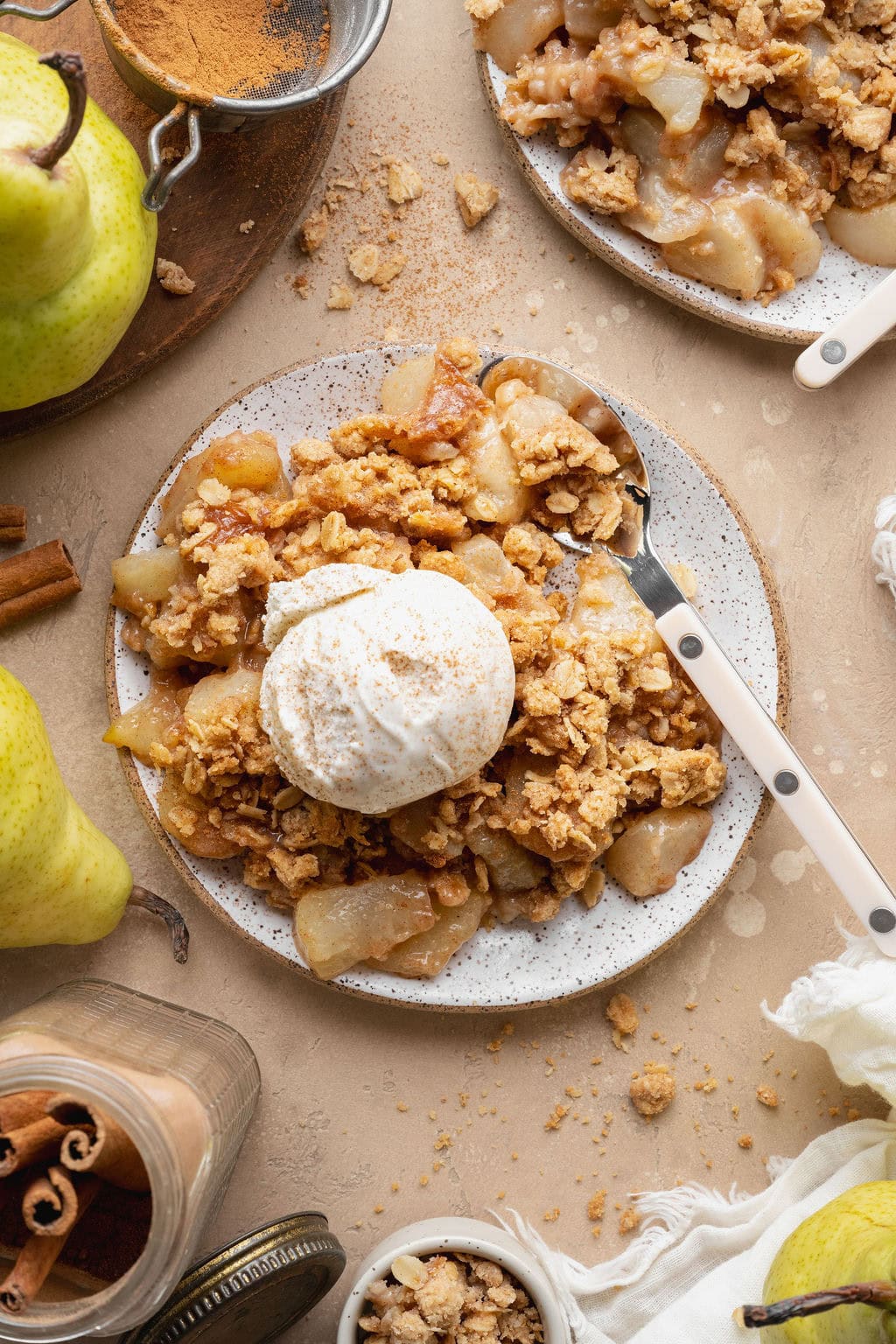 An overhead view of a serving of pear crisp on a plate topped with ice cream, a spoon on the side.